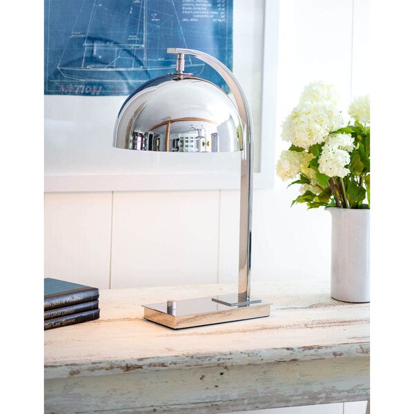 adjustable metal desk lamp on wooden console table with flowers to the right and books on the left